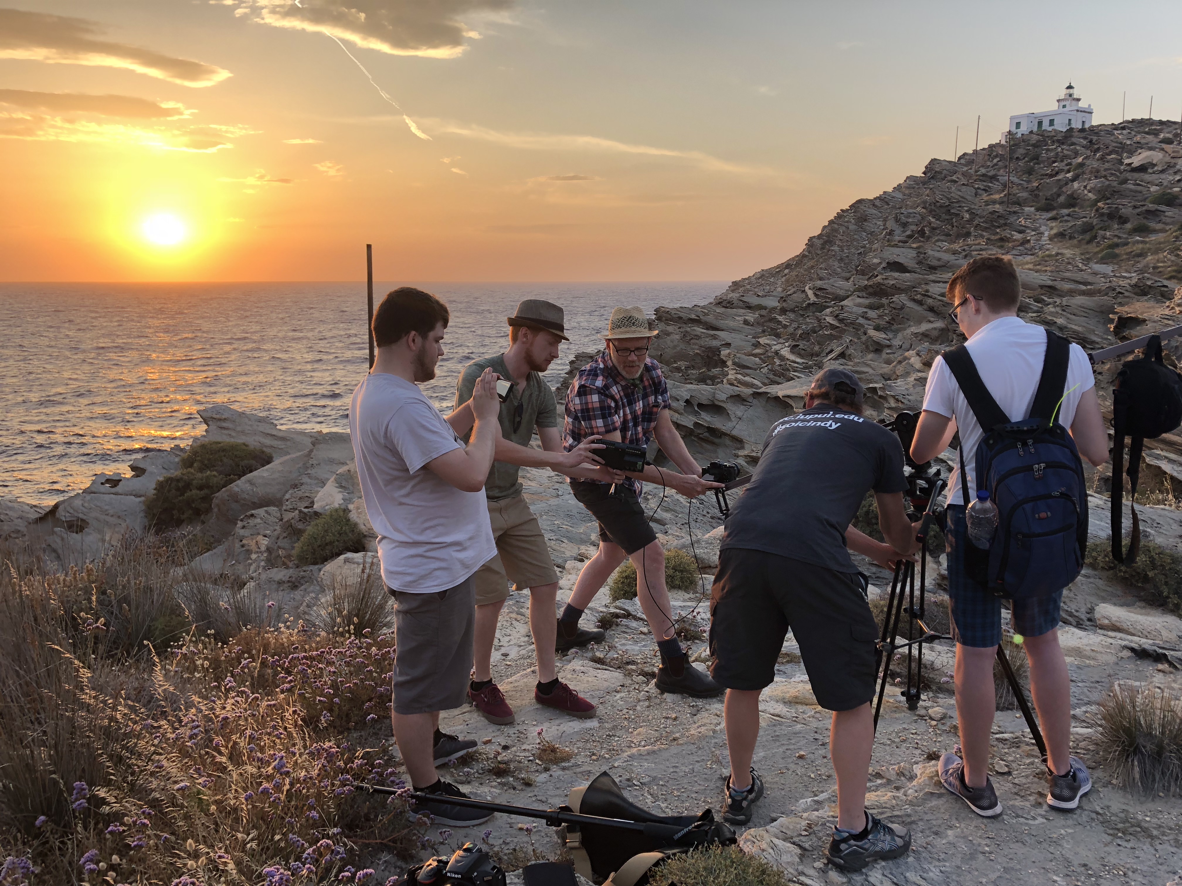 Study Abroad Photo Contest Photo, Students preparing camera for filming on rocky beach in Greece with the sun about to set in the water